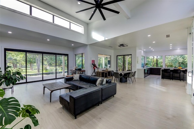 living room featuring a high ceiling, ceiling fan, and light wood-type flooring