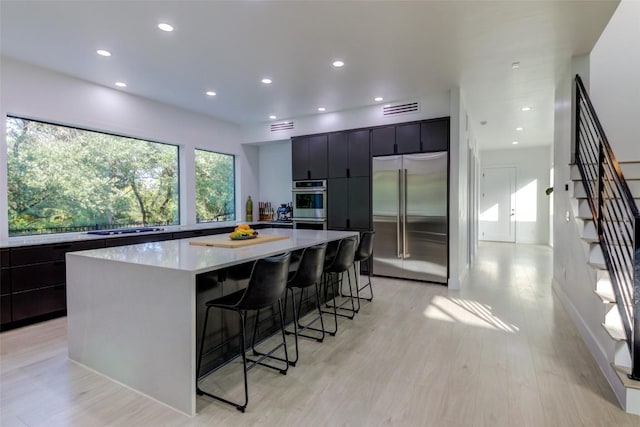 kitchen with a large island, stainless steel appliances, a kitchen breakfast bar, and light wood-type flooring