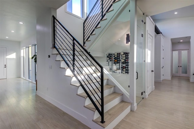 stairs with hardwood / wood-style floors, a towering ceiling, and french doors