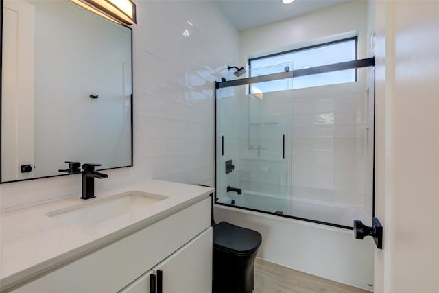 full bathroom with bath / shower combo with glass door, wood-type flooring, vanity, and toilet