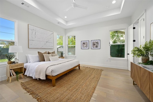 bedroom with a tray ceiling, light hardwood / wood-style floors, and ceiling fan