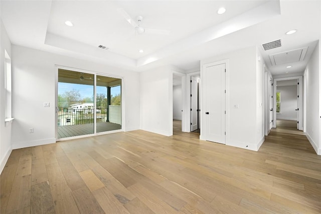 empty room featuring a raised ceiling, ceiling fan, and light wood-type flooring