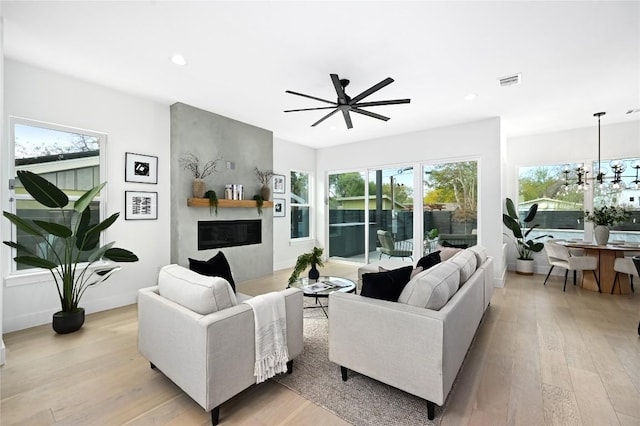 living room featuring ceiling fan with notable chandelier, a fireplace, and light wood-type flooring