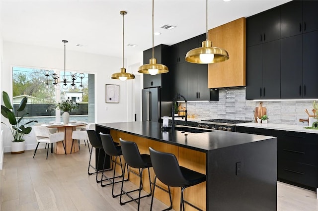 kitchen with sink, hanging light fixtures, high quality fridge, an island with sink, and decorative backsplash