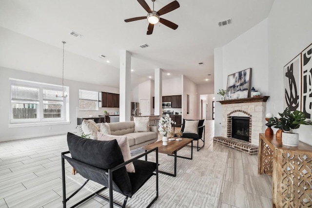 living area featuring ceiling fan with notable chandelier, a brick fireplace, and visible vents