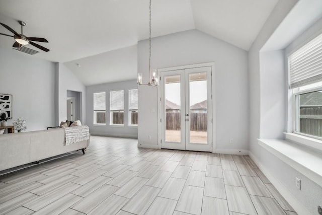 unfurnished living room with baseboards, ceiling fan with notable chandelier, vaulted ceiling, and french doors