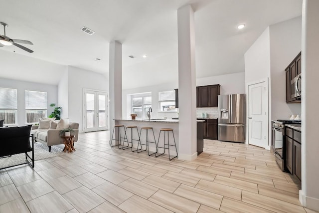 kitchen featuring a breakfast bar, stainless steel appliances, visible vents, open floor plan, and dark brown cabinets