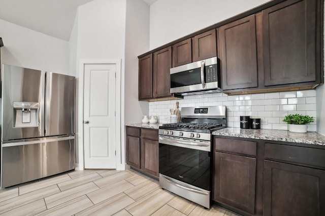 kitchen with stainless steel appliances, light stone counters, backsplash, and dark brown cabinetry