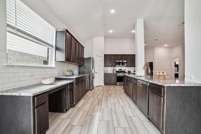 kitchen featuring stainless steel appliances, a sink, dark brown cabinets, light stone countertops, and tasteful backsplash