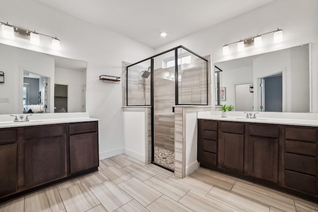 bathroom featuring a stall shower, two vanities, a sink, and baseboards