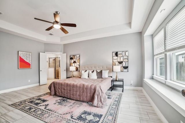 bedroom featuring a tray ceiling, ensuite bath, visible vents, and baseboards