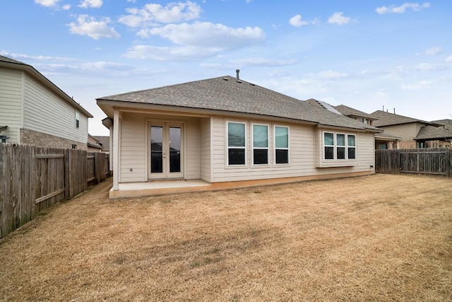 back of property with a lawn, a patio, a fenced backyard, roof with shingles, and french doors