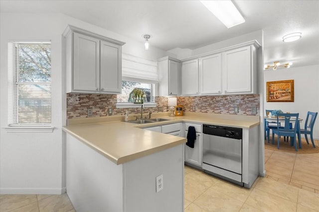 kitchen featuring light tile patterned floors, sink, dishwasher, backsplash, and kitchen peninsula