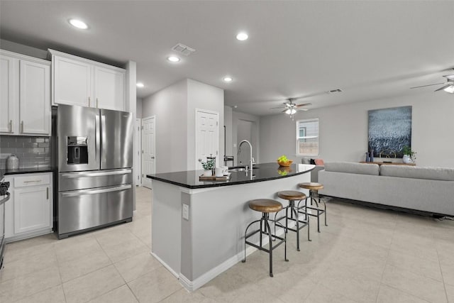 kitchen with a breakfast bar, sink, white cabinets, stainless steel refrigerator with ice dispenser, and a center island with sink