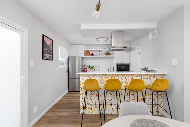 kitchen with white cabinets, a kitchen bar, island exhaust hood, kitchen peninsula, and stainless steel appliances