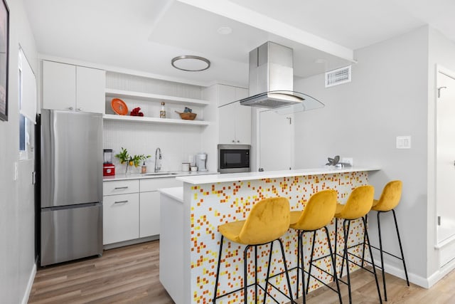 kitchen featuring white cabinetry, island range hood, a kitchen breakfast bar, kitchen peninsula, and stainless steel appliances