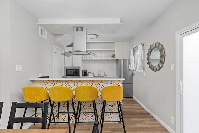 kitchen with appliances with stainless steel finishes, a breakfast bar, island range hood, white cabinetry, and backsplash