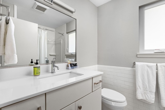 bathroom with vanity, toilet, tile walls, and plenty of natural light