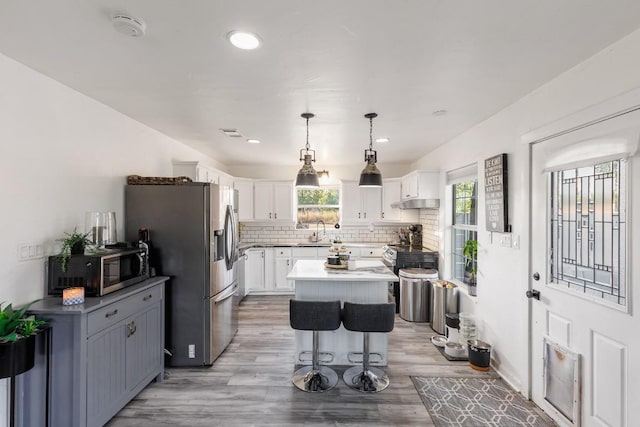 kitchen featuring stainless steel appliances, white cabinetry, a kitchen island, and pendant lighting