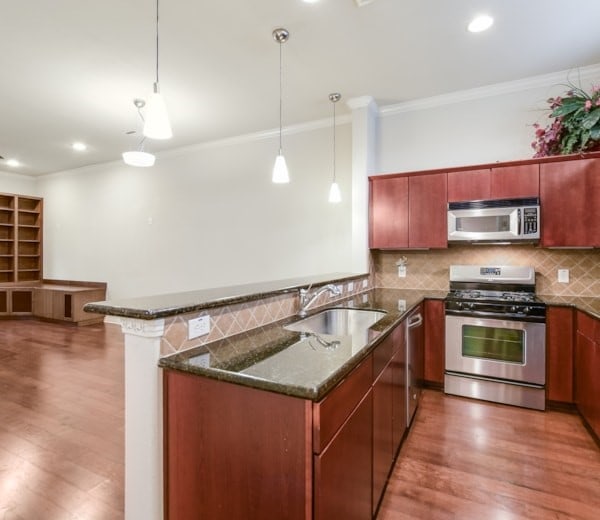 kitchen with appliances with stainless steel finishes, pendant lighting, sink, kitchen peninsula, and crown molding