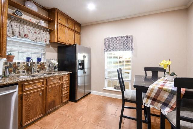 kitchen with stainless steel appliances, sink, ornamental molding, light stone counters, and light tile patterned floors