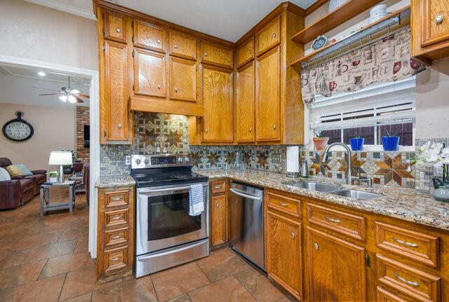 kitchen featuring stainless steel appliances, light stone countertops, ceiling fan, backsplash, and sink