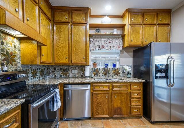 kitchen with ventilation hood, sink, backsplash, light stone counters, and appliances with stainless steel finishes