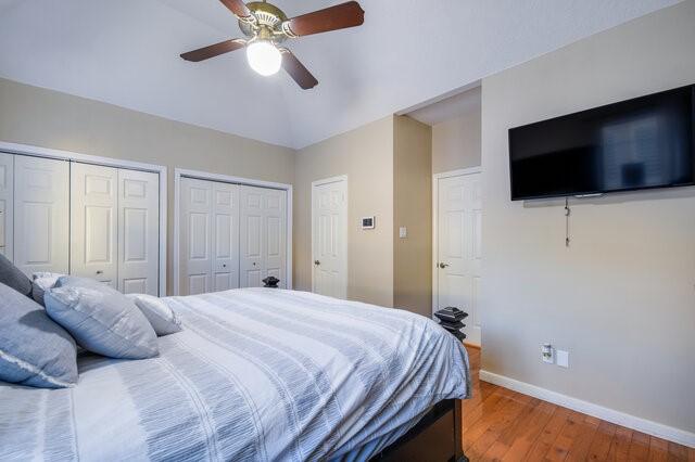 bedroom with ceiling fan, two closets, vaulted ceiling, and wood-type flooring