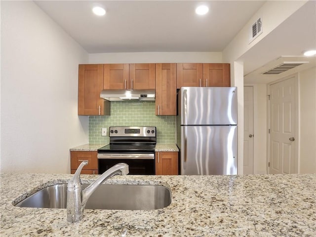 kitchen with sink, decorative backsplash, stainless steel appliances, and light stone countertops