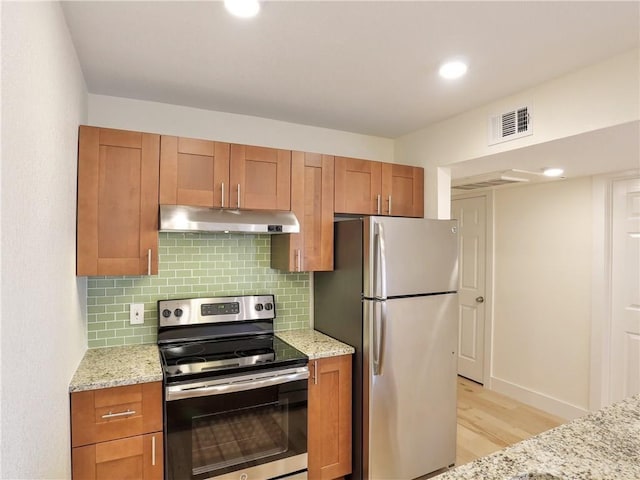 kitchen featuring stainless steel appliances, light stone countertops, decorative backsplash, and light wood-type flooring