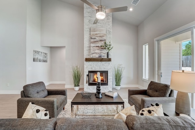 living room featuring ceiling fan, a stone fireplace, high vaulted ceiling, and light wood-type flooring