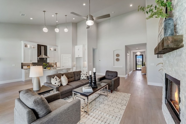 living room featuring ceiling fan, a towering ceiling, a fireplace, and light hardwood / wood-style floors