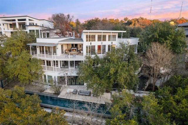 back house at dusk featuring a balcony, a sunroom, and a patio area