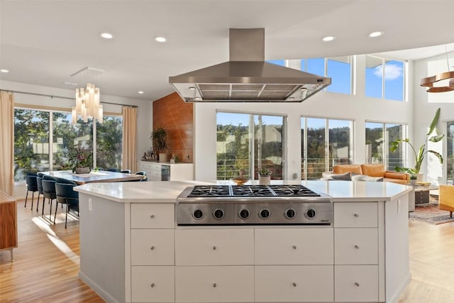 kitchen with island exhaust hood, stainless steel gas stovetop, a kitchen island, and white cabinets