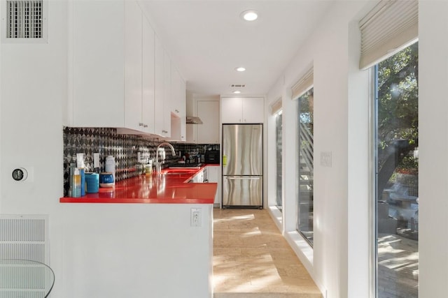 kitchen with sink, stainless steel fridge, white cabinetry, decorative backsplash, and light wood-type flooring