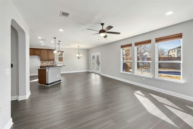 unfurnished living room featuring sink, ceiling fan with notable chandelier, and dark wood-type flooring