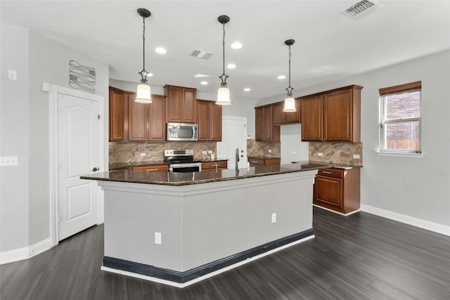 kitchen featuring decorative light fixtures, dark stone countertops, decorative backsplash, stainless steel appliances, and a center island with sink