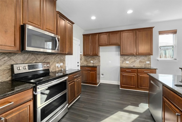 kitchen featuring dark wood-type flooring, appliances with stainless steel finishes, decorative backsplash, and dark stone counters