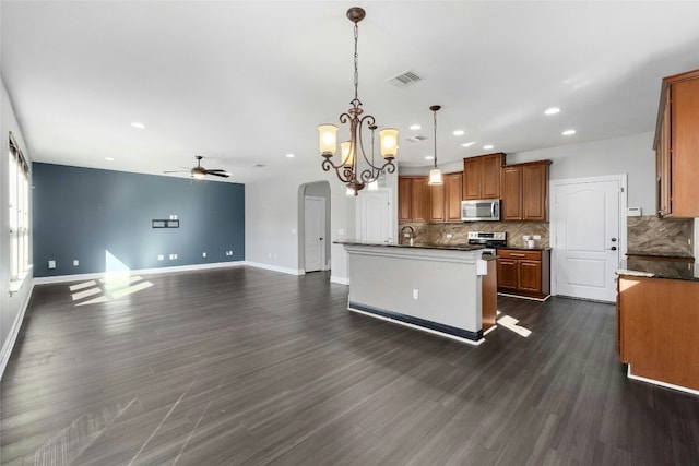 kitchen featuring decorative backsplash, stainless steel appliances, hanging light fixtures, and a center island with sink