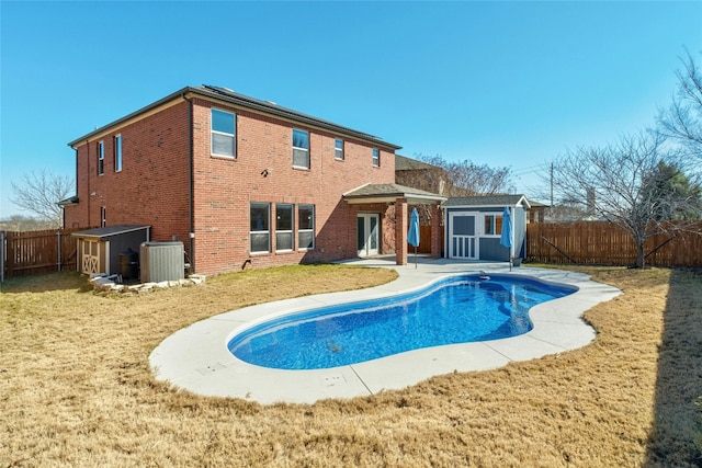 rear view of house with a storage shed, central AC unit, a lawn, and a fenced in pool