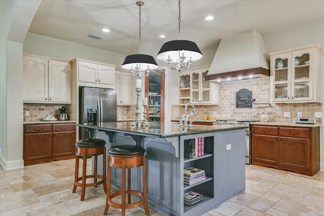 kitchen with premium range hood, hanging light fixtures, a center island with sink, dark stone countertops, and appliances with stainless steel finishes