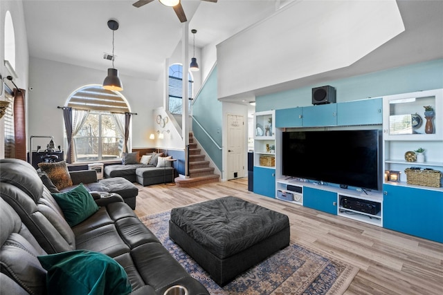 living room with ceiling fan, a towering ceiling, and light hardwood / wood-style floors