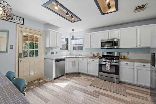 kitchen with pendant lighting, light hardwood / wood-style floors, white cabinets, and appliances with stainless steel finishes