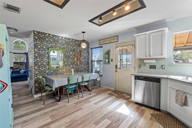 kitchen with hanging light fixtures, stainless steel dishwasher, white cabinets, and light wood-type flooring