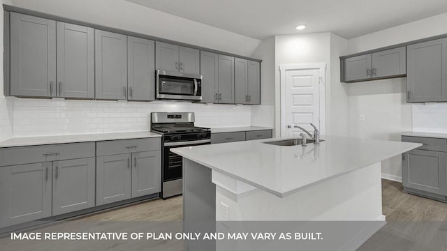 kitchen with sink, gray cabinetry, a kitchen island with sink, stainless steel appliances, and light wood-type flooring