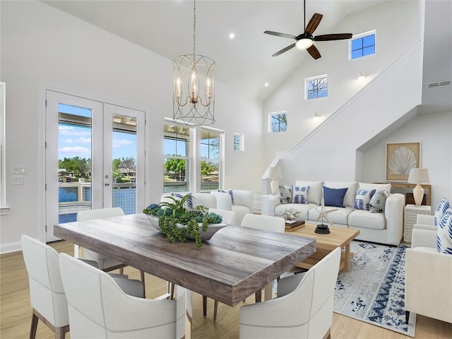 dining room with french doors, ceiling fan with notable chandelier, high vaulted ceiling, and light hardwood / wood-style flooring