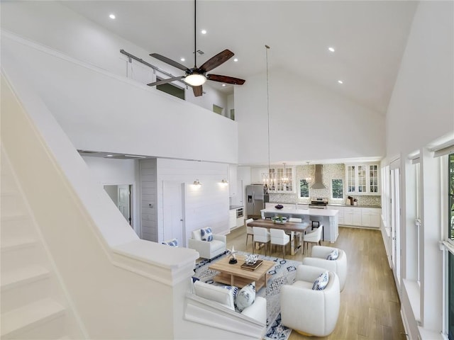 living room featuring high vaulted ceiling, ceiling fan with notable chandelier, and light hardwood / wood-style flooring