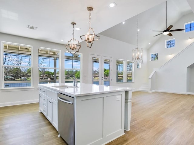 kitchen featuring decorative light fixtures, white cabinetry, an island with sink, sink, and stainless steel dishwasher