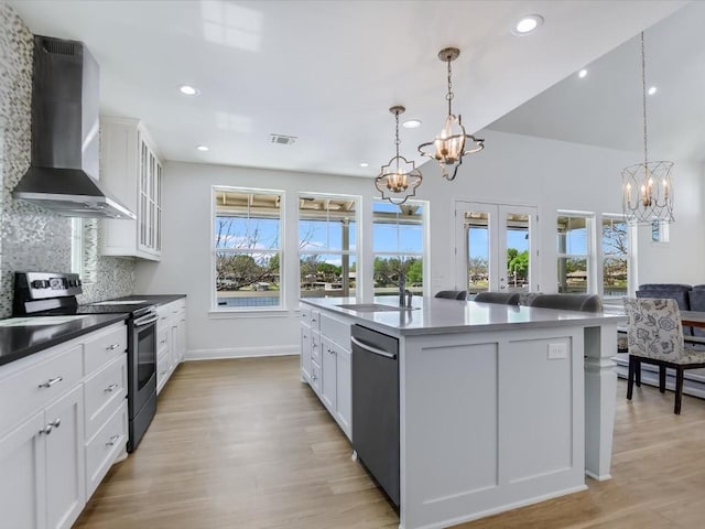 kitchen with pendant lighting, wall chimney range hood, sink, appliances with stainless steel finishes, and a kitchen island with sink