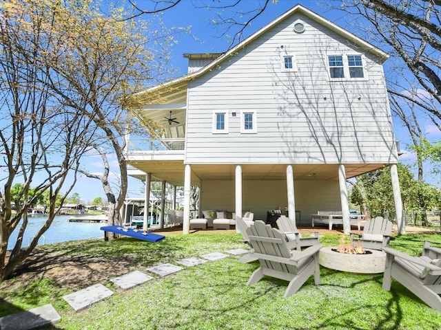 rear view of property with a water view, a yard, an outdoor living space with a fire pit, and ceiling fan